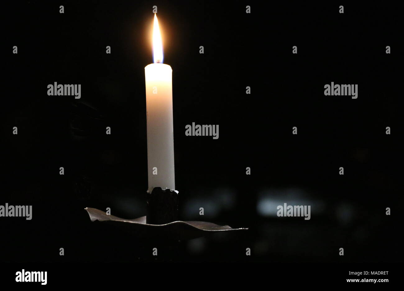A single candle glows against a dark, black background. Stock Photo