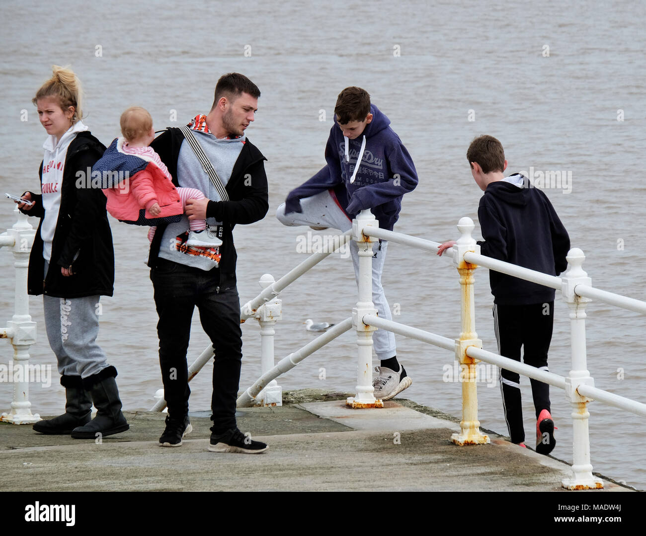 Family group with two youths in danger on wrong side of sea wall railings. Stock Photo