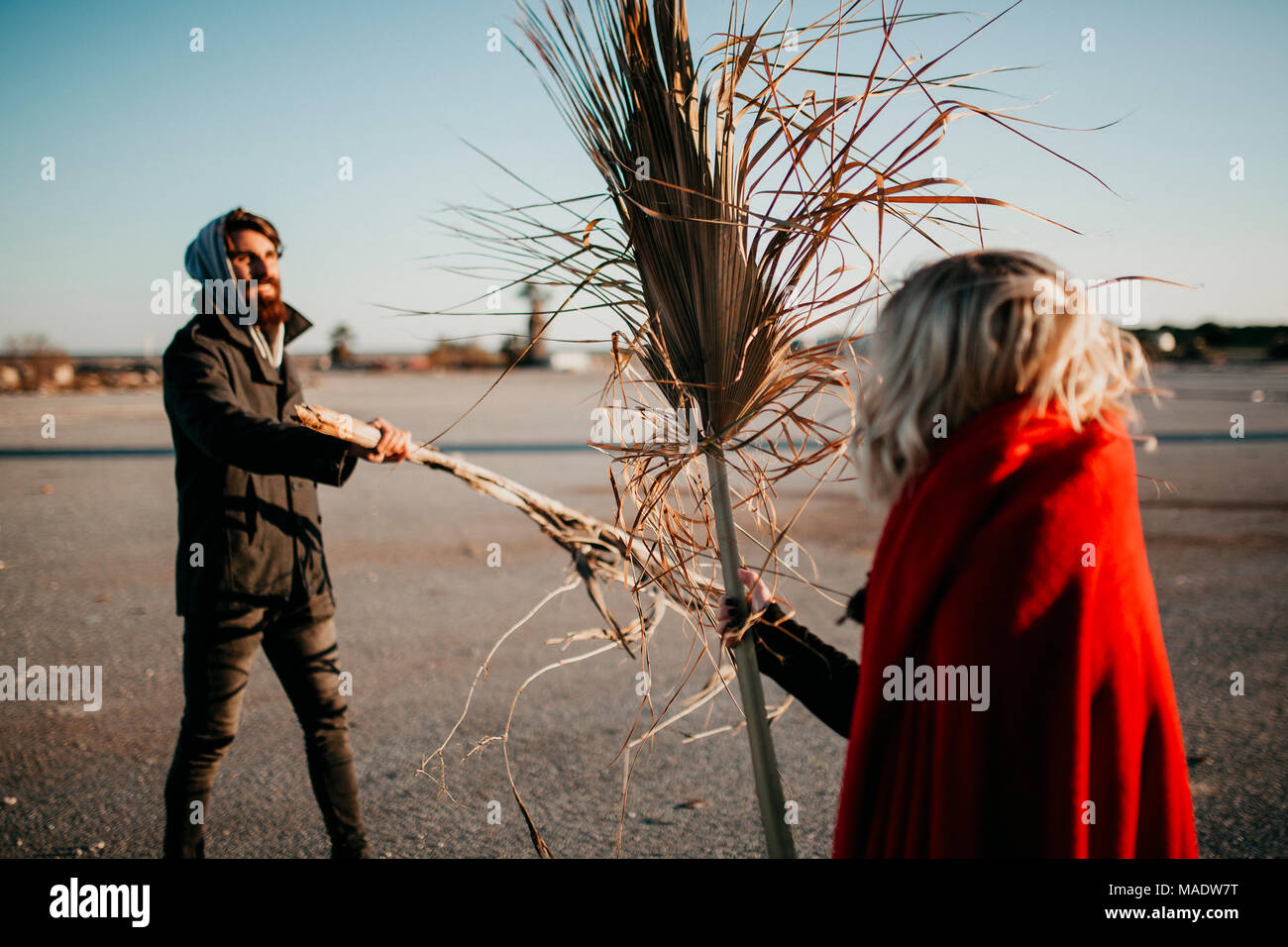 Cool hipster couple playing and battling with plant branches outdoors at sunset. Stock Photo