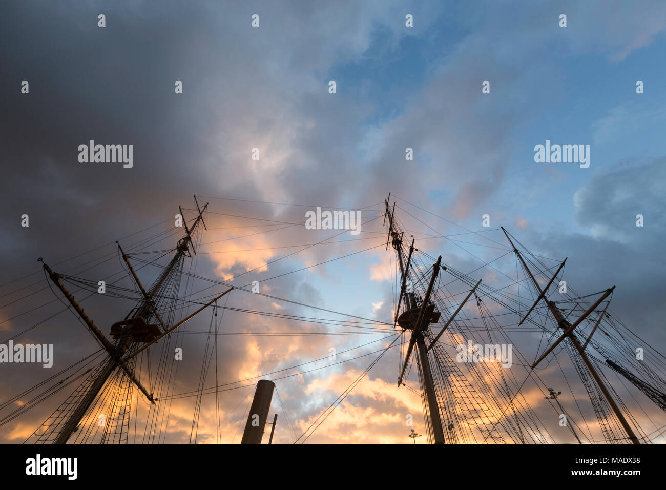 Vibrant orange clouds in a dramatic sky above the wooden masts of HMS Gannet at The Historic Dockyard, Chatham, Kent, UK just before sunset. Stock Photo