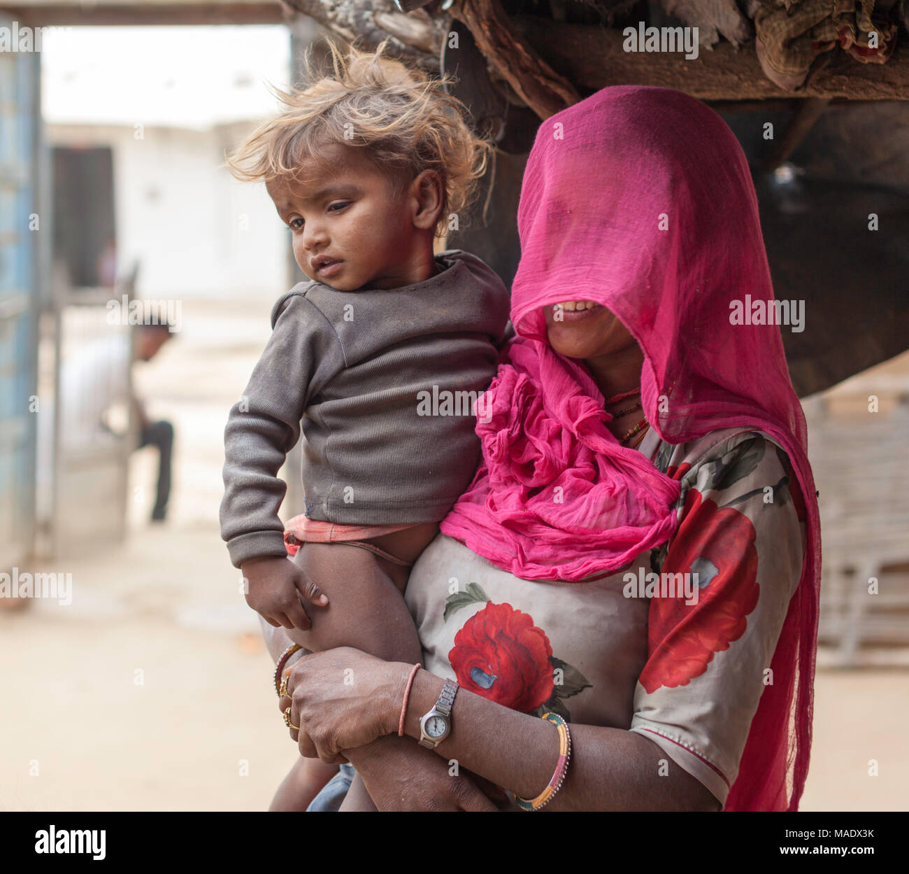 Woman with her head covered by a pink scarf holds a young child in a traditional village near Shapura, Rajasthan, India. Stock Photo