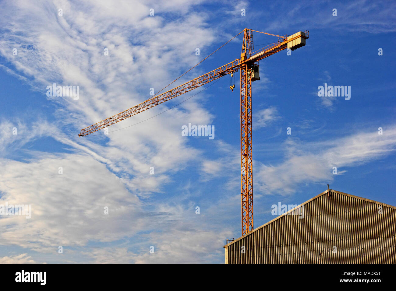 Crane towers over building against cloudy blue sky Stock Photo - Alamy