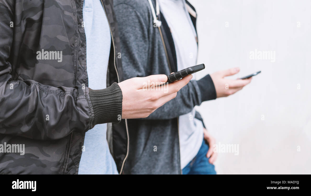 two unrecognizable mobile phone addicted male teenagers using smartphone Stock Photo