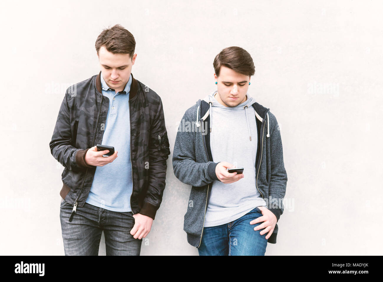 two antisocial mobile phone addicted male teenagers looking at their smartphone Stock Photo