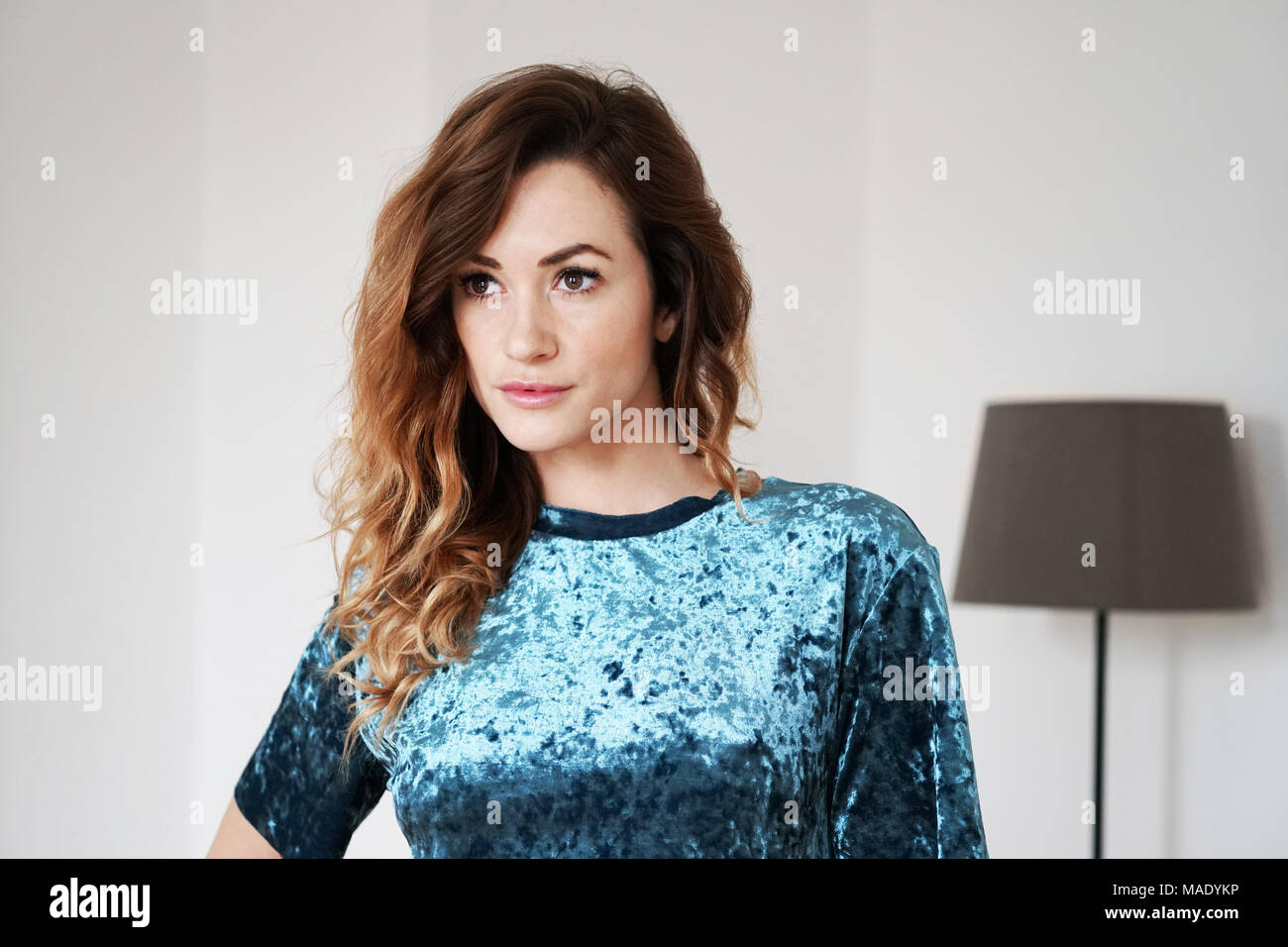 young woman is lost in thought standing in living room with floor lamp Stock Photo