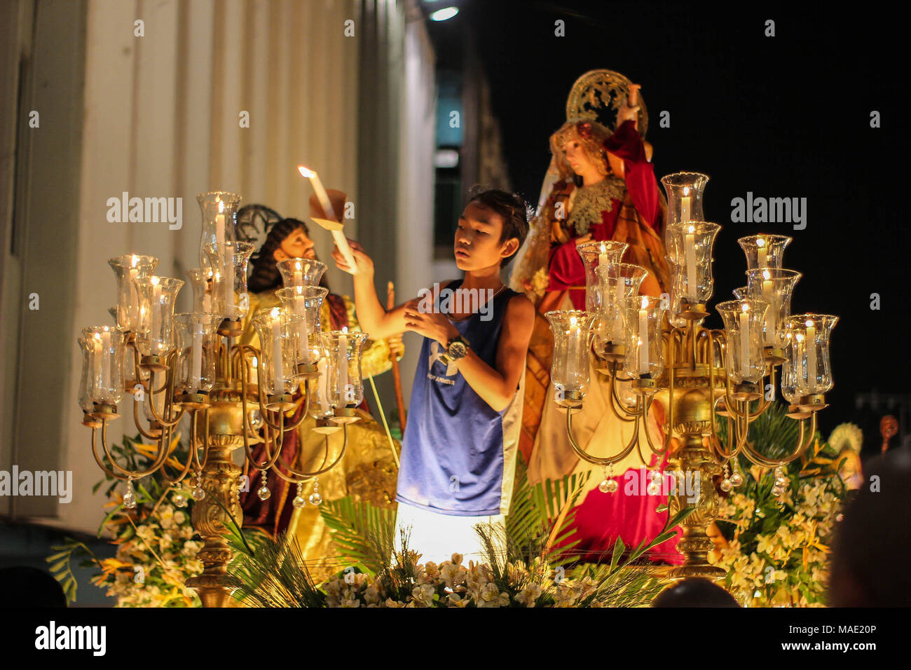 March 29, 2018 - Manila, NCR, Philippines - A young boy giving light to the candles of their float during the parade..Every year of in March, Christians all over the world commemorate the suffering and death of Jesus Christ on the cross. In the Philippines, Holy Week or â€œSemana Santaâ€ has been celebrated by having different rituals and practices such as â€œVisita Iglesiaâ€ or visiting several churches, â€œPenetensyaâ€ or Penitence of re enacting the hardship of Jesus Christ, â€œPabasaâ€ or graphical reading of the word of God and â€œParadaâ€ or parade of the saints, disciple and journe Stock Photo