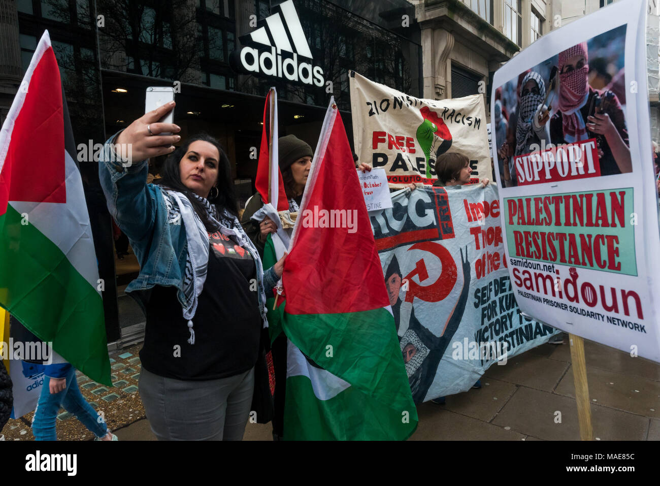 March 31, 2018 - London, UK. 31st March 2018. A protester takes a selfie  outside Adidas on the rolling protest along Oxford St in solidarity with  Gaza and the Land Day protests