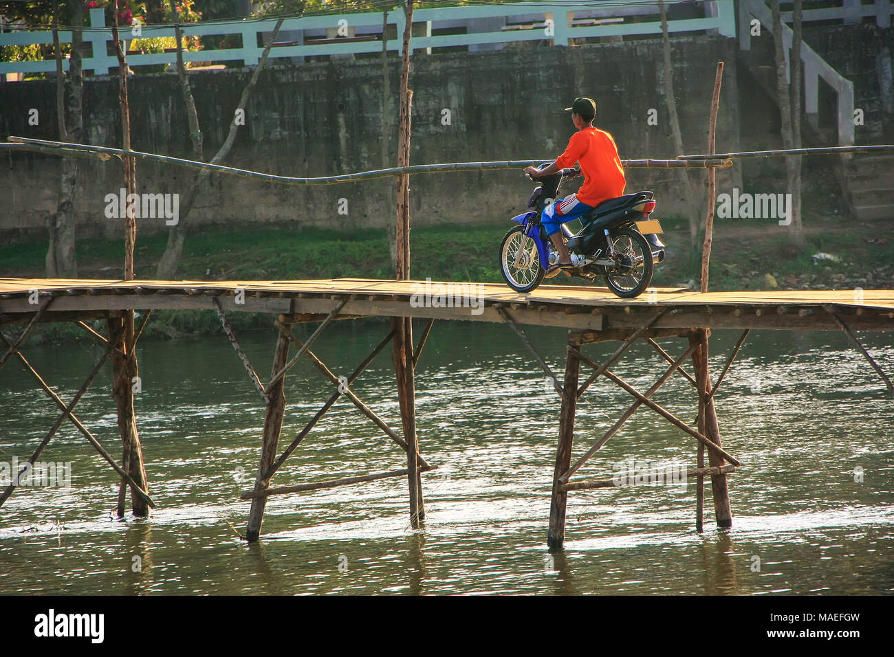Local man riding motorbike on the bridge in Vang Vieng, Laos. Vang Vieng is a tourist-oriented town in Vientiane Province. Stock Photo