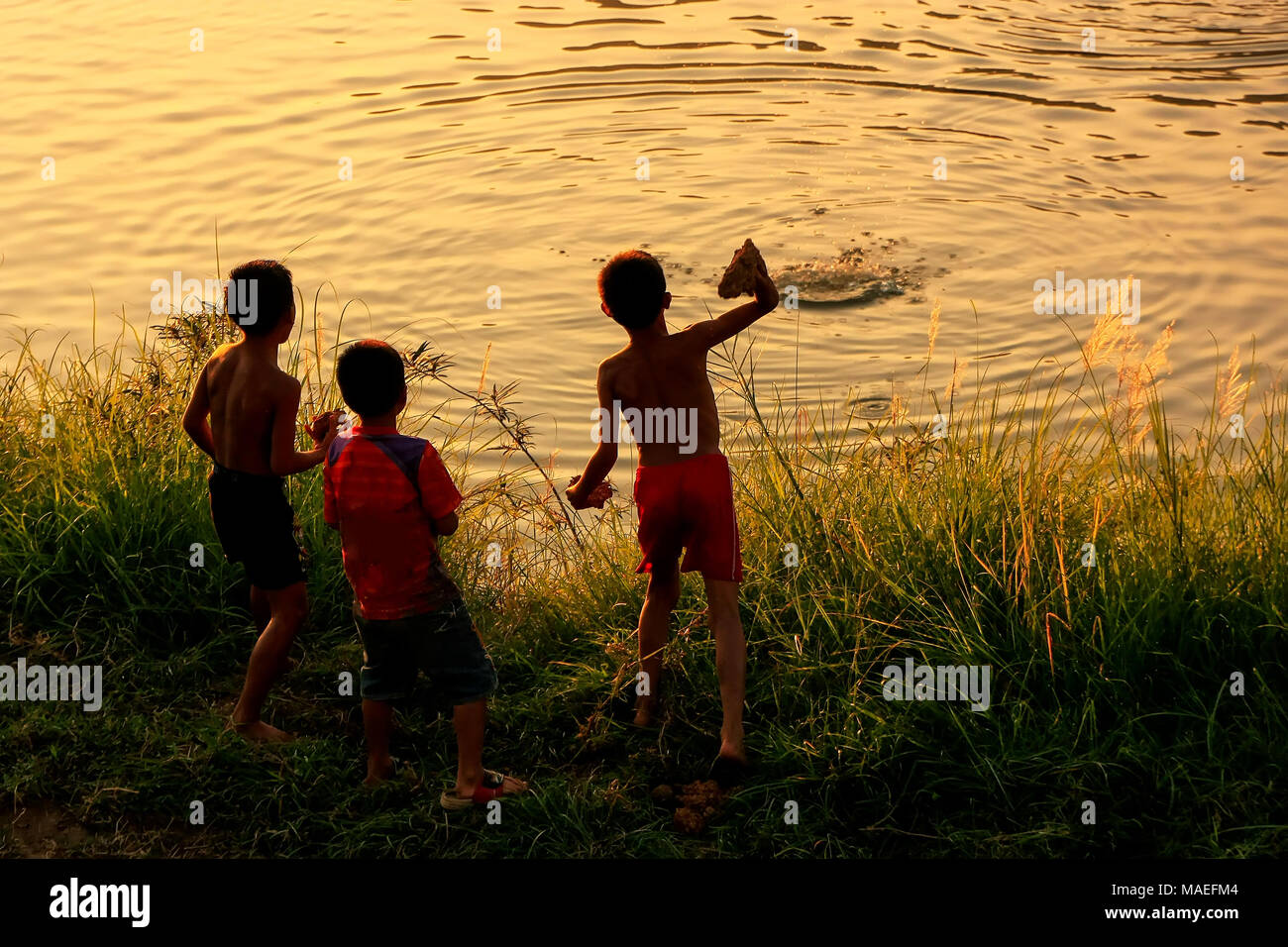 Local kids throwing rocks in Nam Song River at sunset, Vang Vieng, Laos. Vang Vieng is a popular destination for adventure tourism in a limestone kar Stock Photo