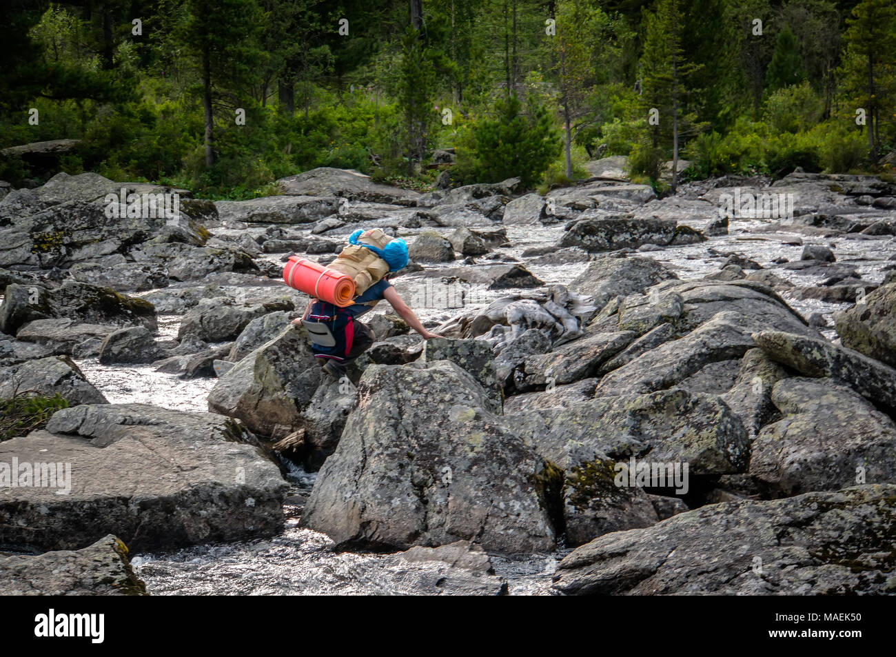Hiker man with backpack crossing a river on stones in bulgarian mountains. Stock Photo