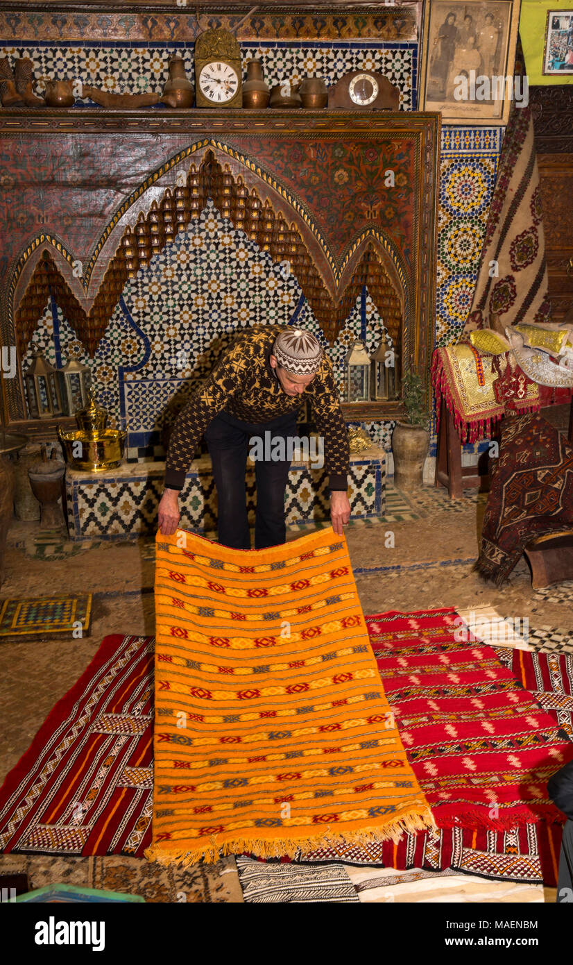 Morocco, Fes, Fes el Bali, Medina, antiques shop, salesman displaying colourful carpets Stock Photo
