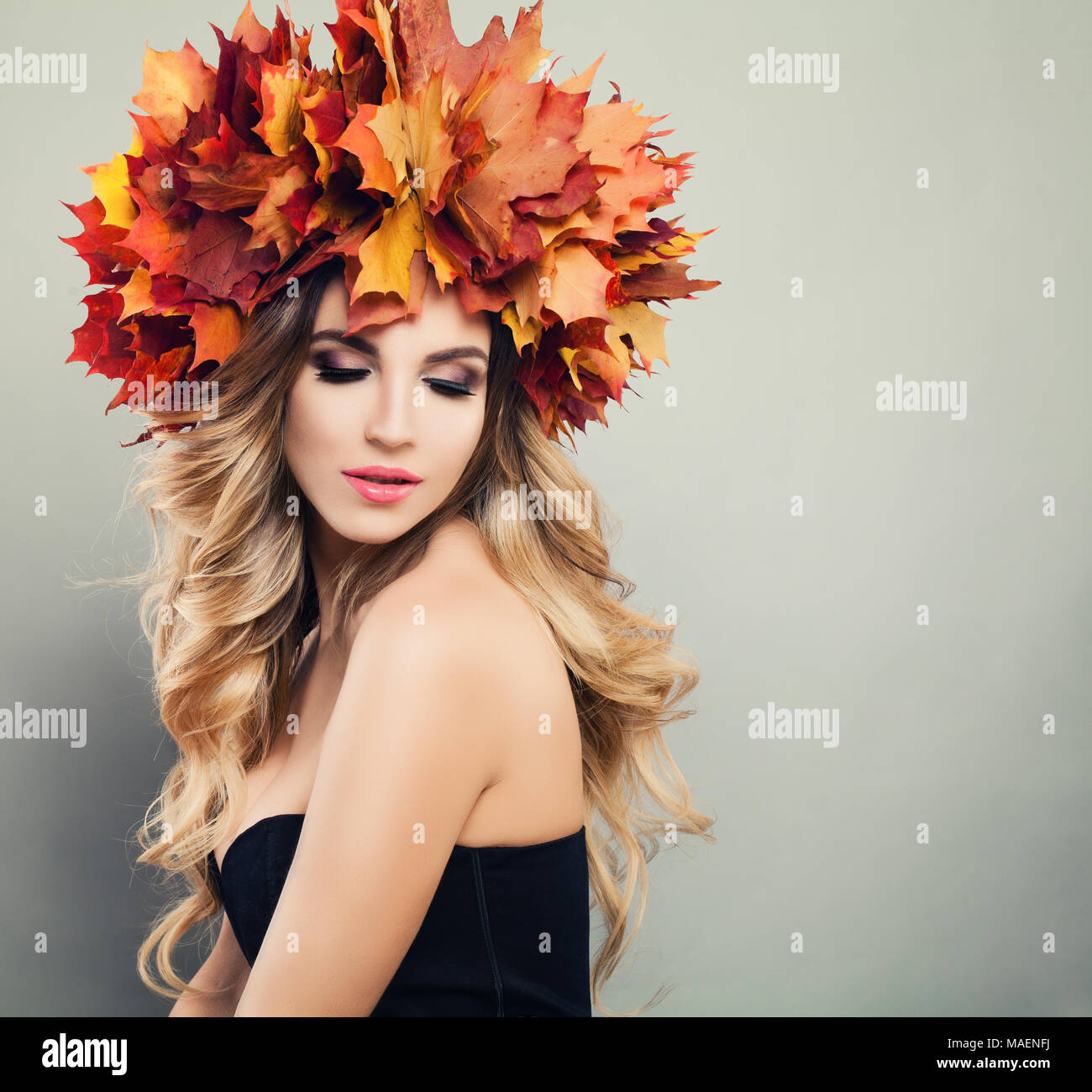 Autumn Beauty. Beautiful Woman Spa Model with Wavy Blonde Hair, Makeup and Fall Leaves Wreath on Gray Background with Copy space Stock Photo