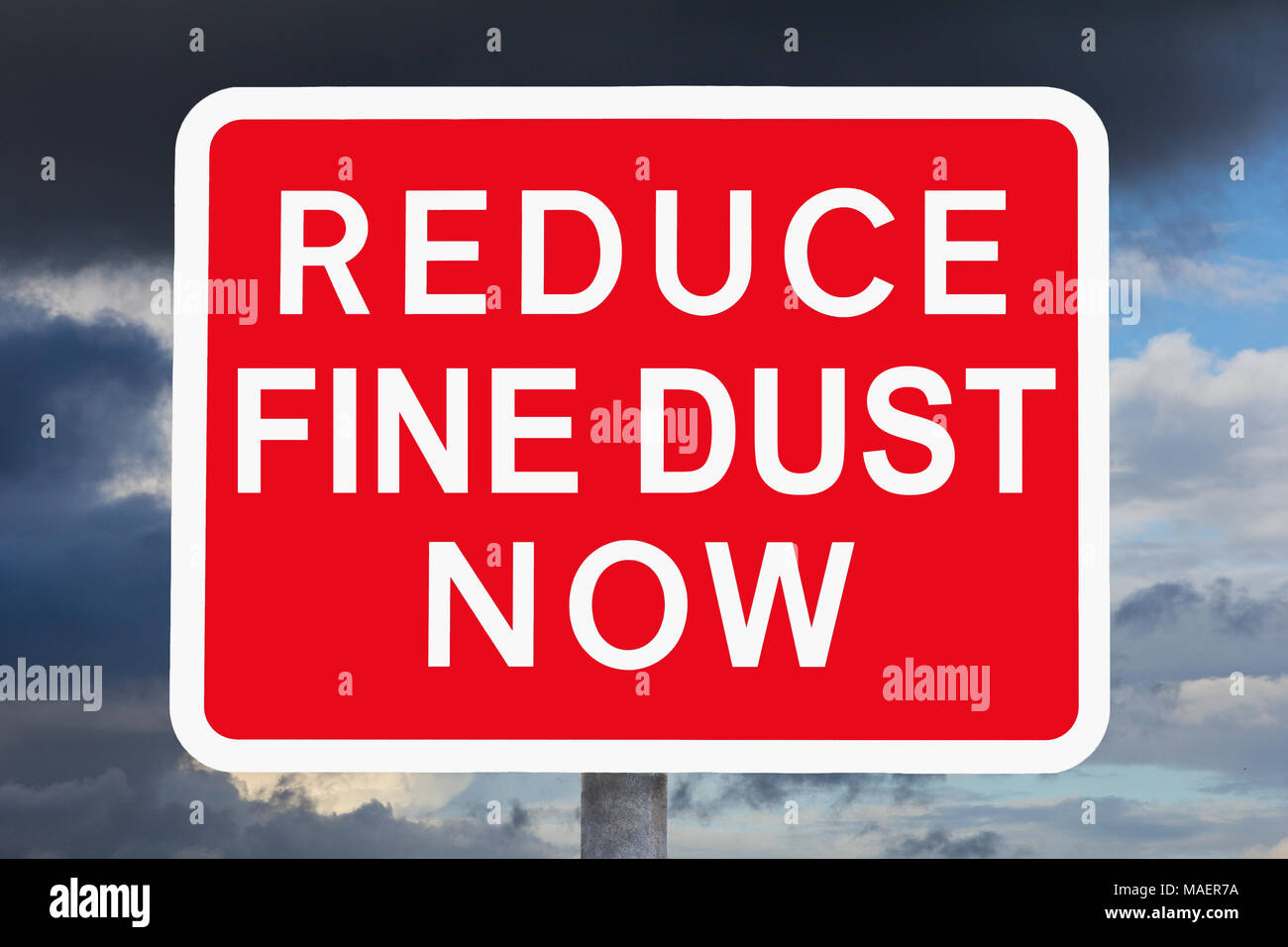 Red and white warning sign REDUCE FINE DUST NOW in front of a sky with very dark clouds, variation of a british traffic sign. Stock Photo