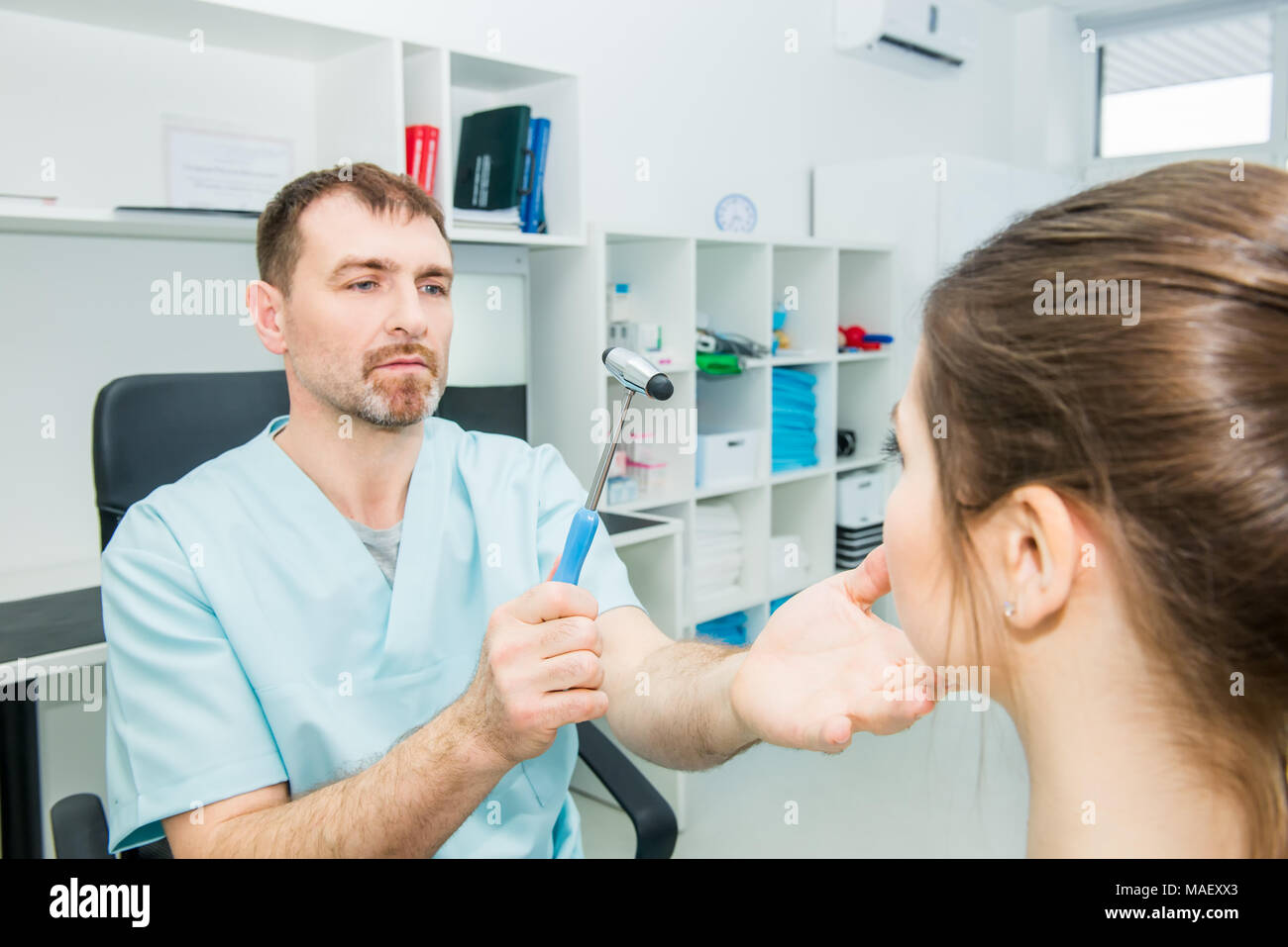 Male neurologist doctor inspecting young female patient's nervous system using a hammer. Neurological physical examination. Helthcare and medicine con Stock Photo