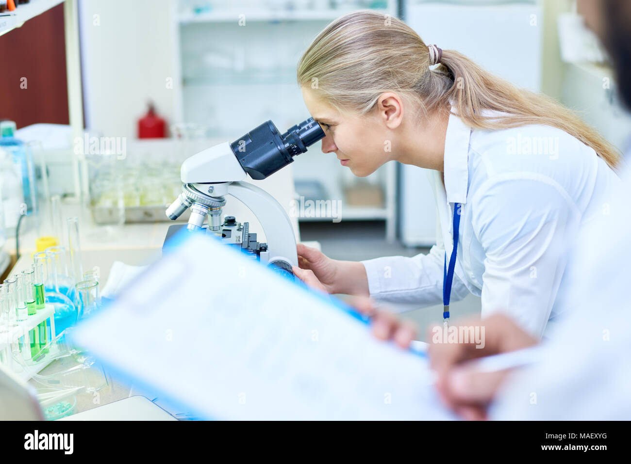 Serious medical student analyzing sample through microscope Stock Photo