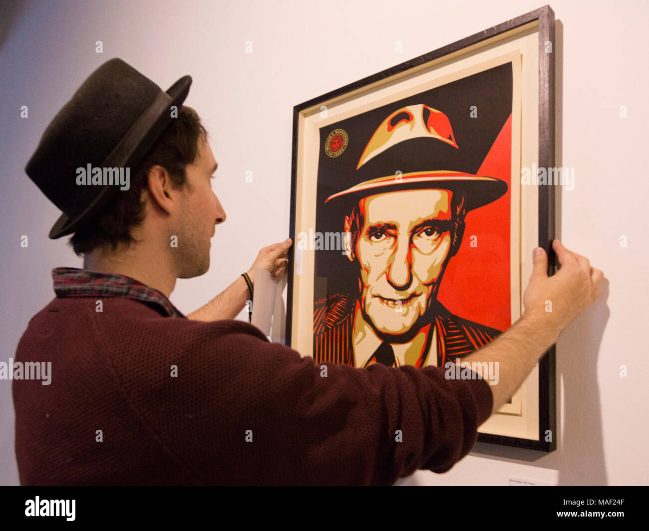 London, UK. 28 August 2014.  Curator James Elphick straightens the screenprint picture 'Burroughs 100 Years' by Kate Simon and Shepard Fairey. The 'Animals in the Wall' exhibition showcases a new side to iconic American writer and creative mind Willam S Burroughs. The exhibition features 40 original Burroughs artworks and never before shown pieces of contributing artists. 'Animals in the Wall' is curated by James Elphick and Yuri Zumancic and runs from 29 August 20 to 7 September 2014 at the Londonewcastle Project Space in Redchurch Street, Spitalfields, London. Stock Photo
