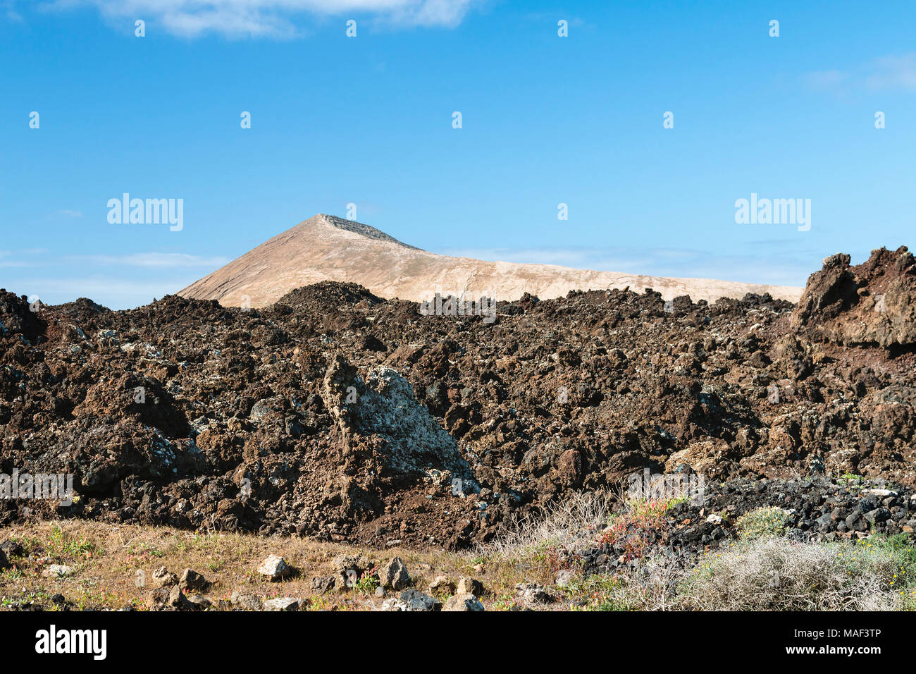The lava field Lavas Negras in front of the Montana Tinache near Tinajo in Lanzarote, Spain with blue sky. Stock Photo