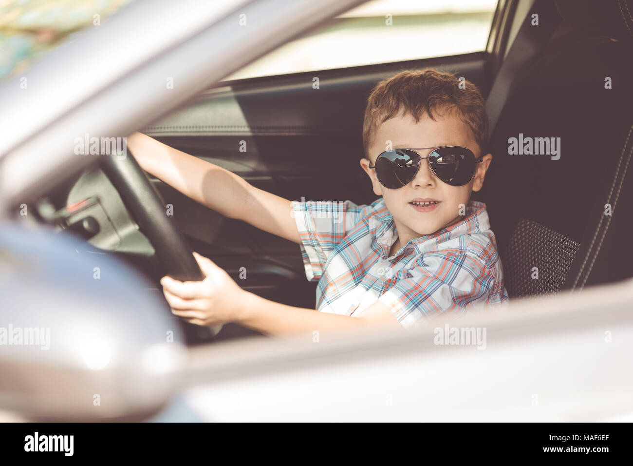 One happy little boy sitting in the car at the day time. Concept of summer vacation. Stock Photo