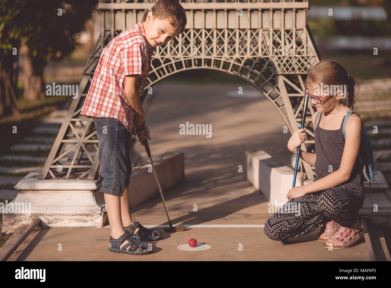 Happy brother and sisters  playing mini golf in a park at the day time. People having fun otdoors. Concept of good leisure. Stock Photo