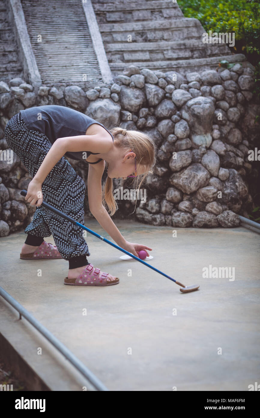 Happy little girl  playing mini golf  playing mini golf in a park at the day time. Kid having fun outdoors. Concept of good leisure. Stock Photo