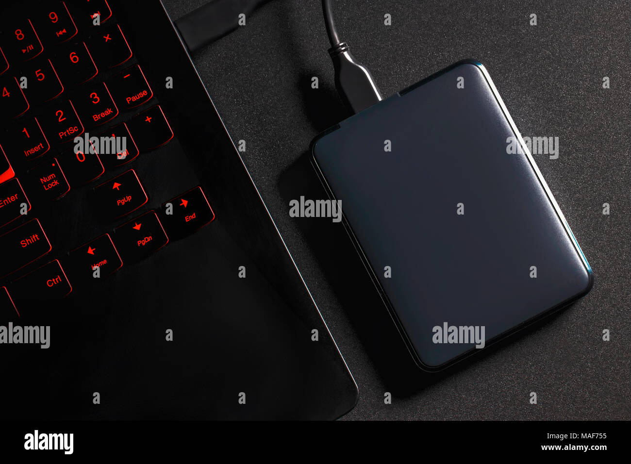 An external hard drive connected to the laptop with a usb cable on a black background. Stock Photo