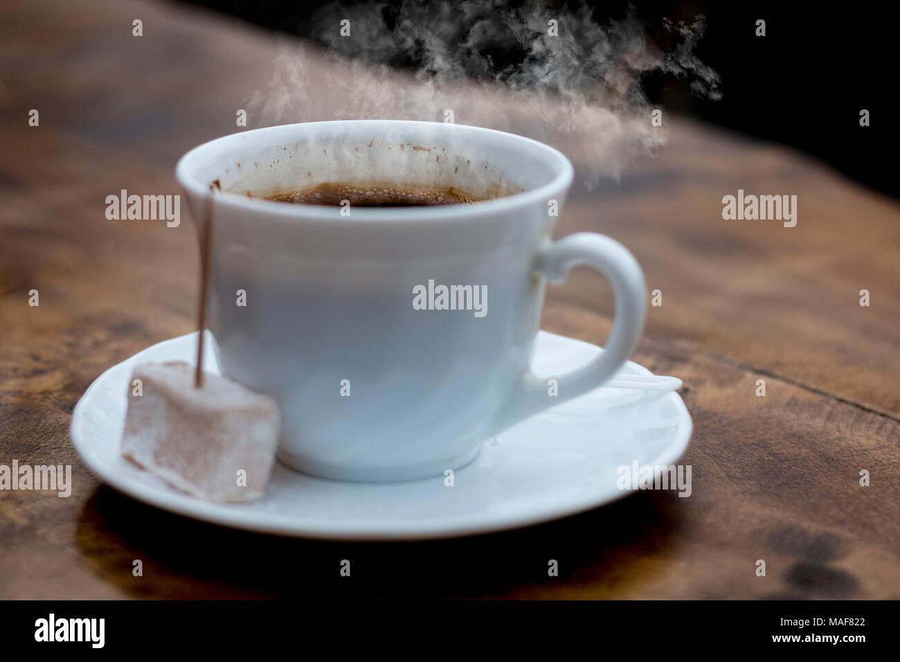 Steaming cup of Turkish coffee served with locum with tootpick in it, wood table, dark background and great contrast Stock Photo