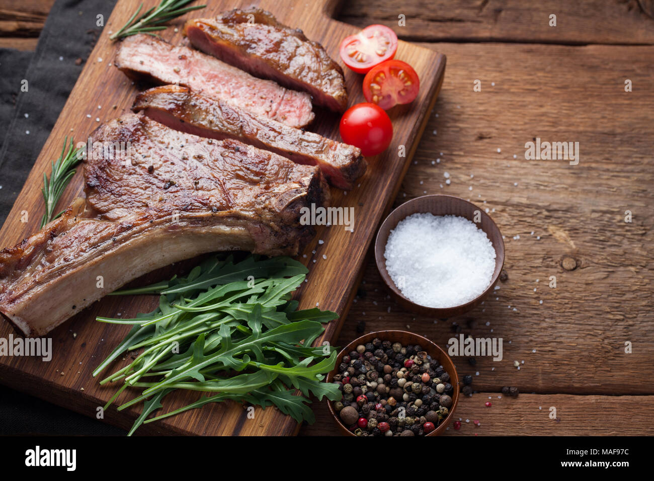 Grilled cowboy beef steak, herbs and spices on a rustic wooden background. Top view with copy space for your text. Stock Photo