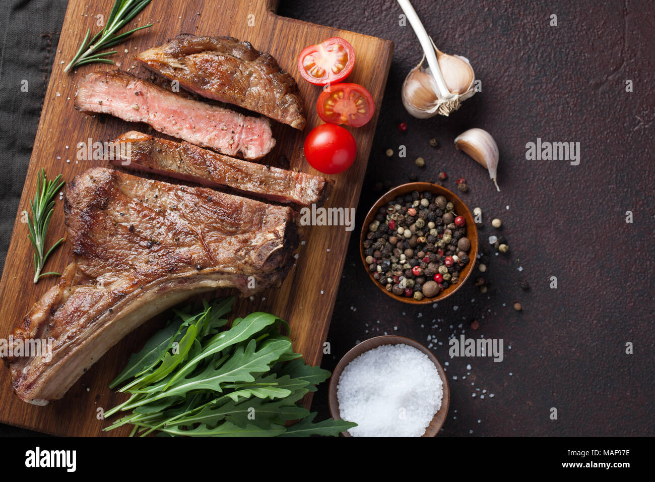 Grilled cowboy beef steak, herbs and spices on a dark stone background. Top view with copy space for your text. Stock Photo