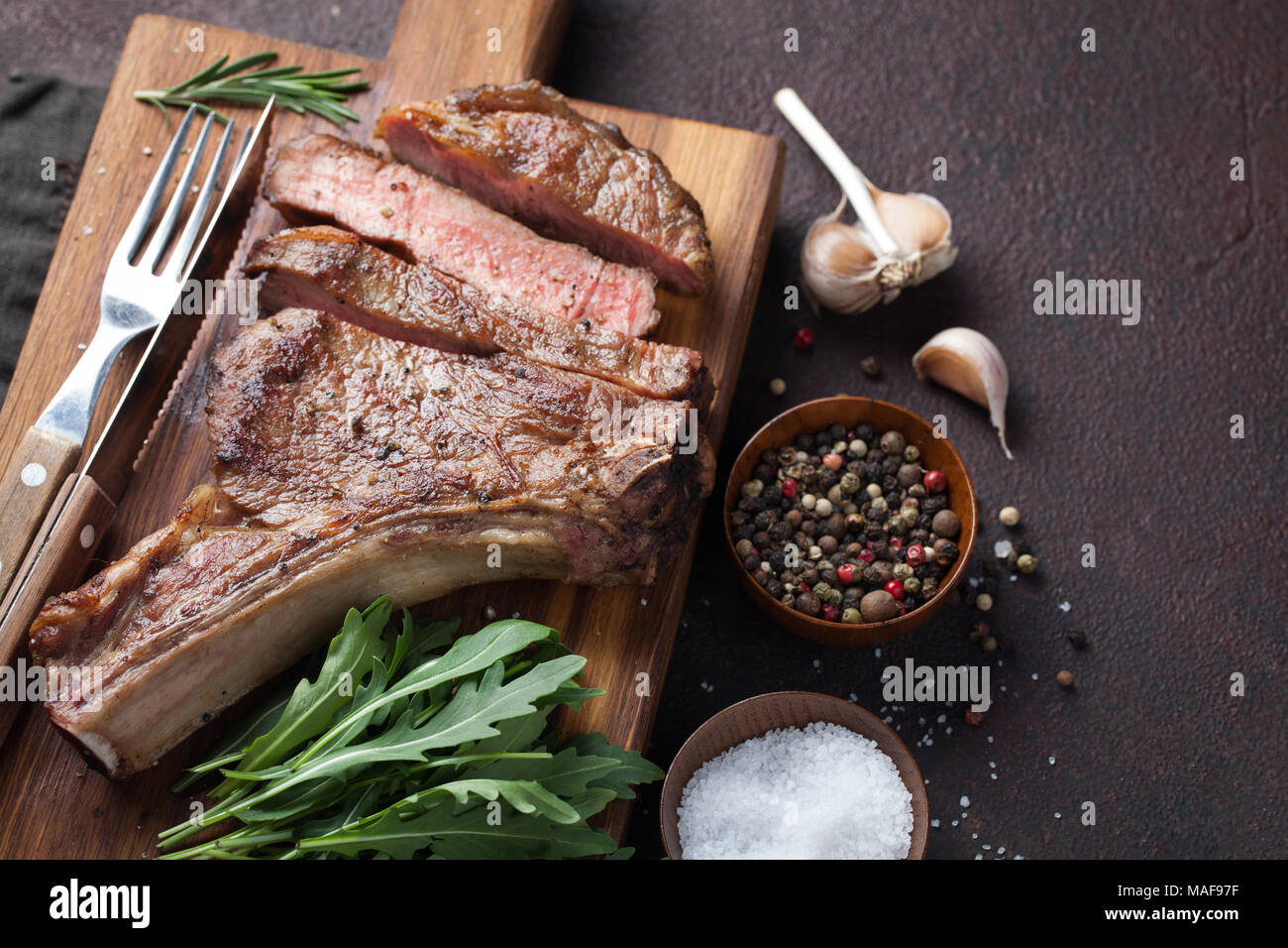 Grilled cowboy beef steak, herbs and spices on a dark stone background. Top view. Stock Photo