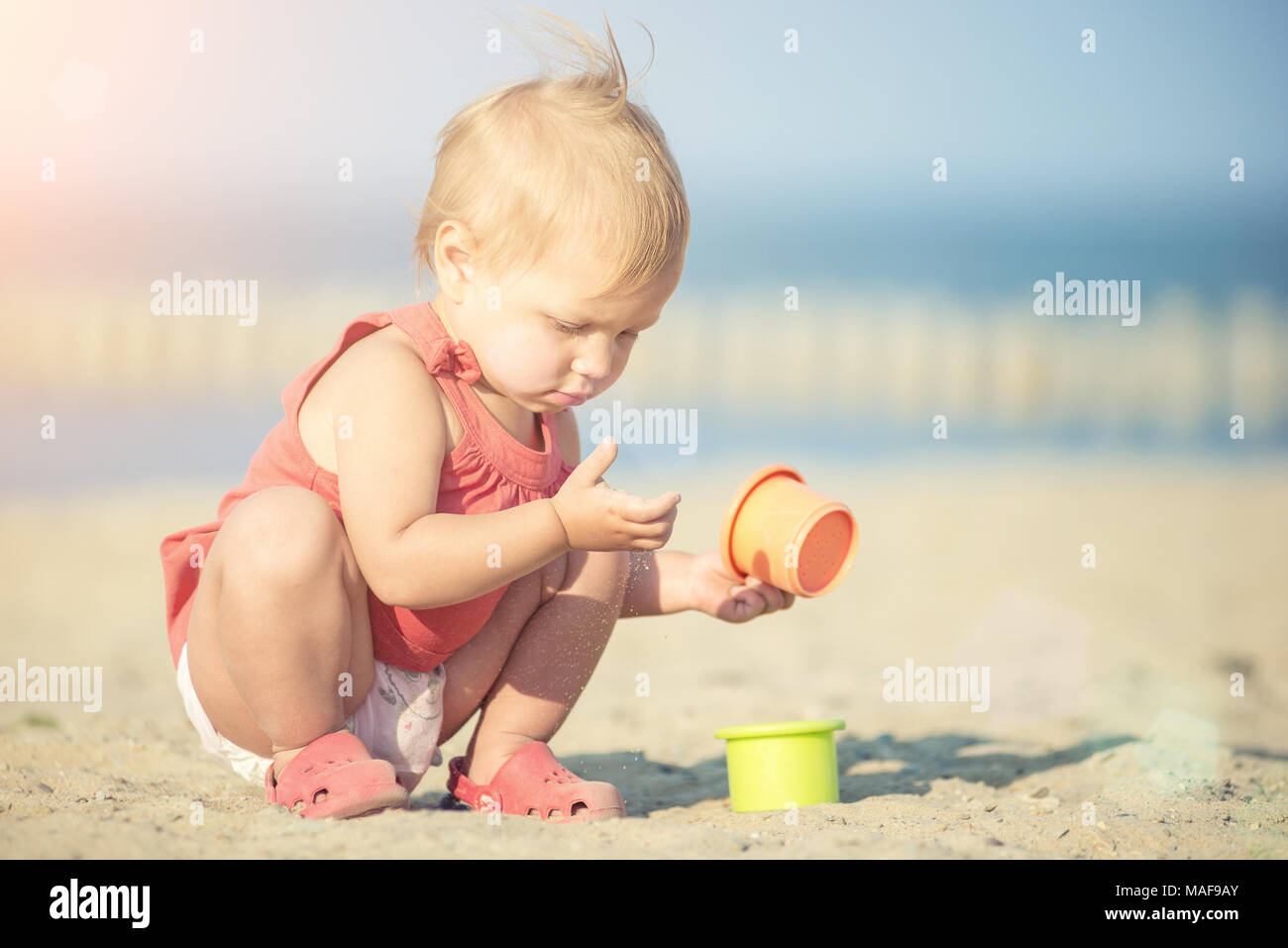 Baby girl in red dress playing on sandy beach near the sea Stock Photo ...