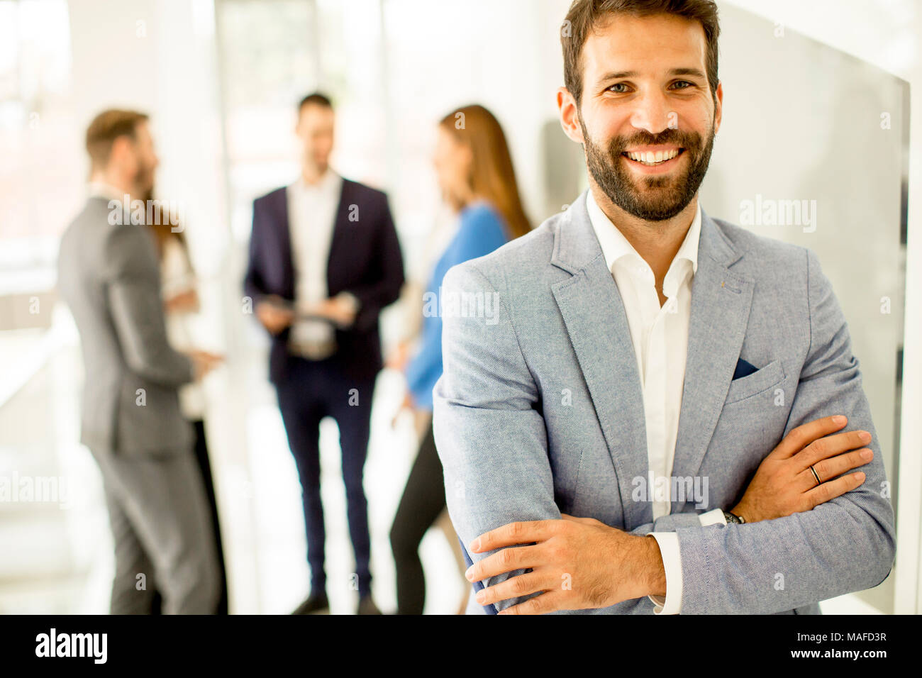 Young businessman standing in the office and other young business people talking in the background Stock Photo