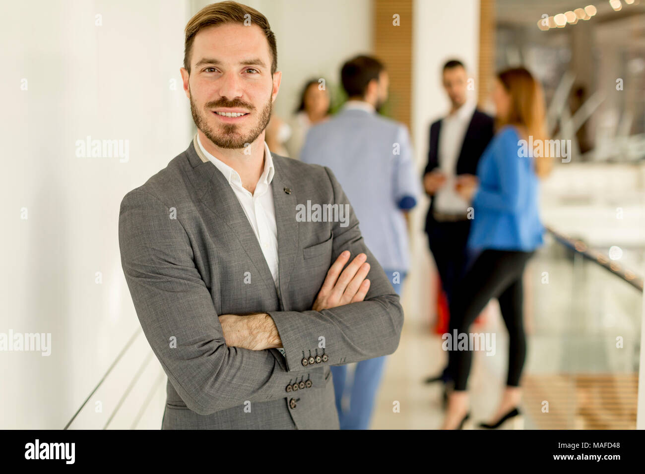 Young businessman standing in the office and other young business people talking in the background Stock Photo