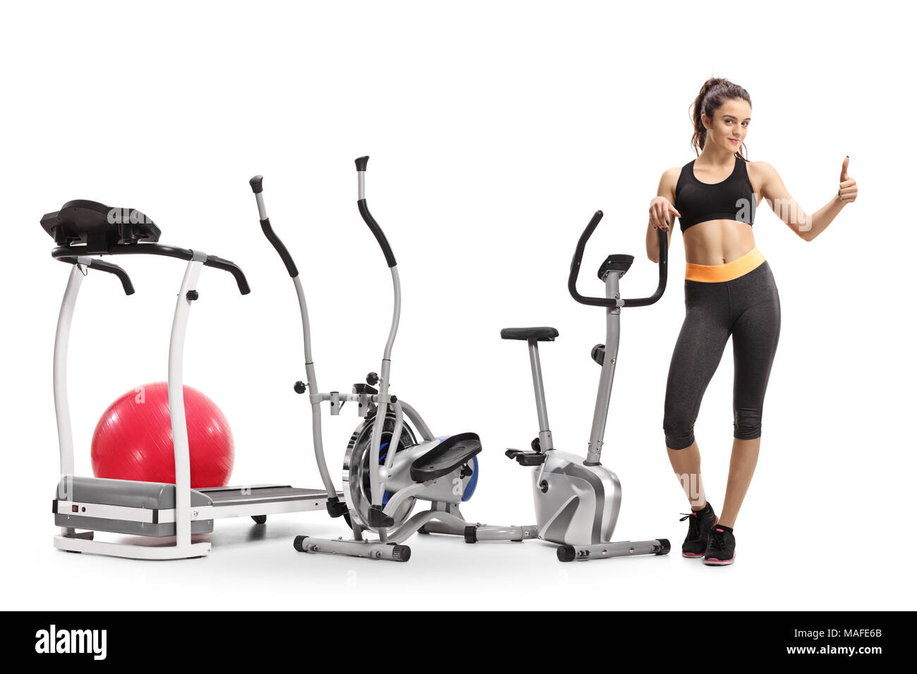 Full length portrait of a fitness girl standing by exercise machines and making a thumb up gesture isolated on white background Stock Photo