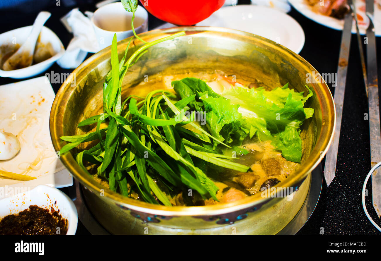 Chopsticks inserting fresh vegetable into hotpot Stock Photo