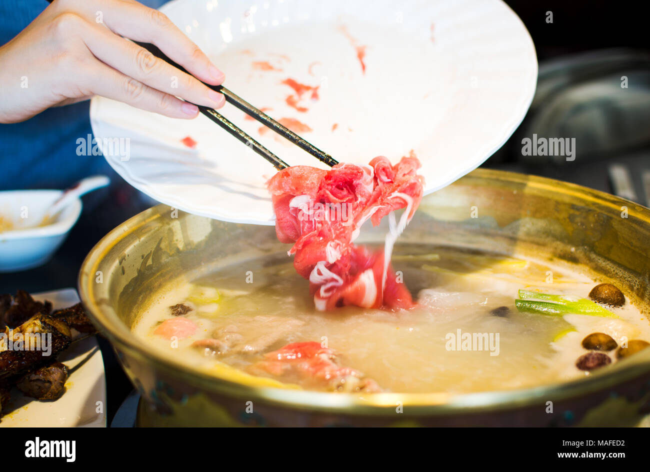 Chopsticks inserting sliced lamb into boiling hotpot Stock Photo