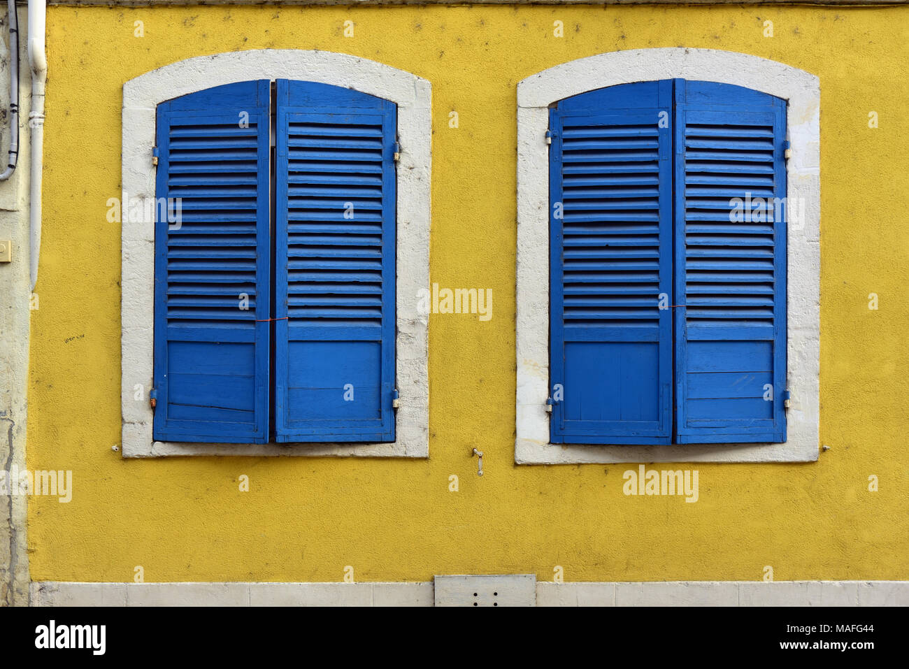 Closed blue window shutters and a yellow wall in Verdun, France Stock Photo