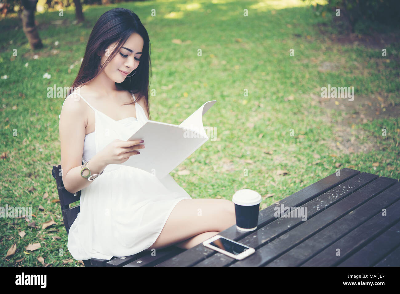 Young beautiful woman sitting and reading the book in the park ...
