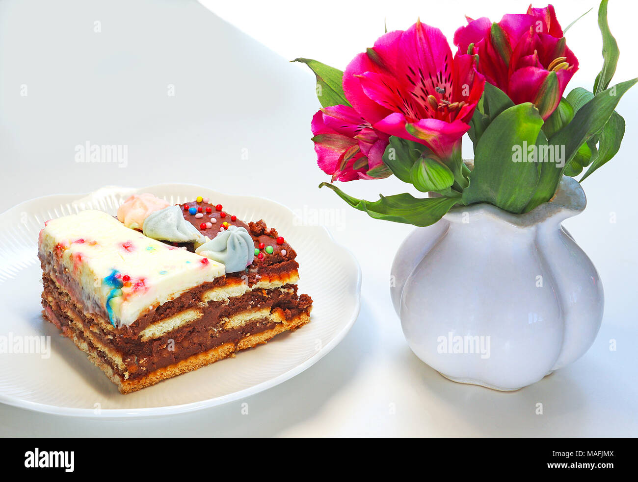 Close up of a slice colorful decorated biscuit cake and flowers Stock Photo