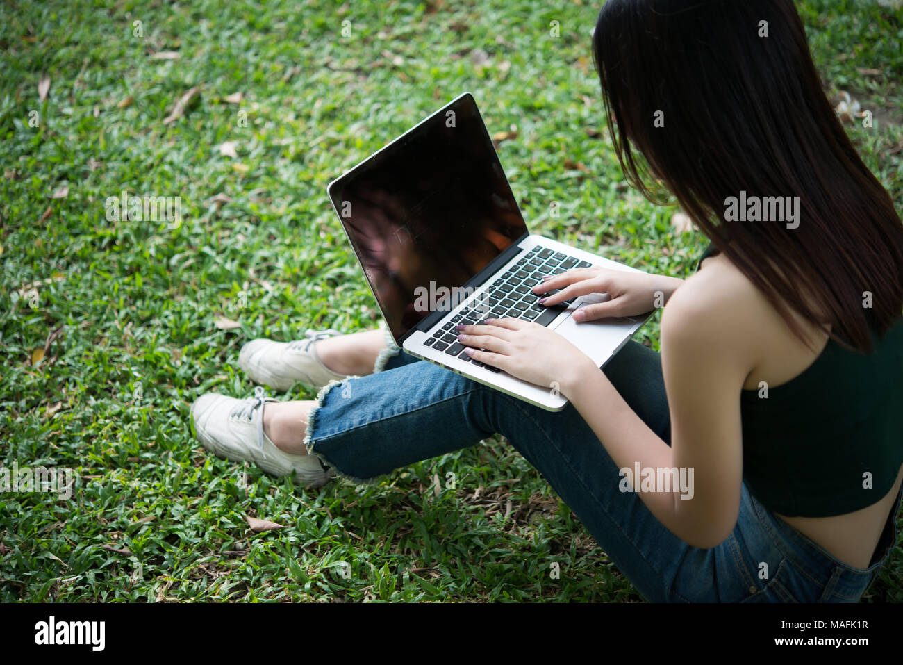 Young beautiful woman sitting on green grass and using laptop in the ...