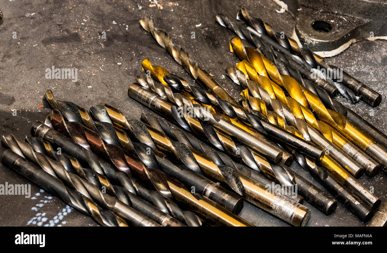 Assorted used drill bits laying on a steel table with grime Stock Photo