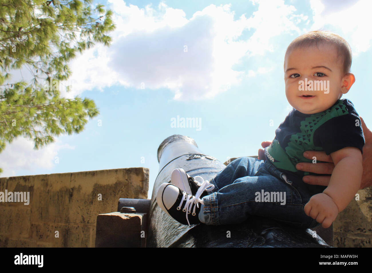 Six months old baby boy sitting on canon with help from dady Stock Photo