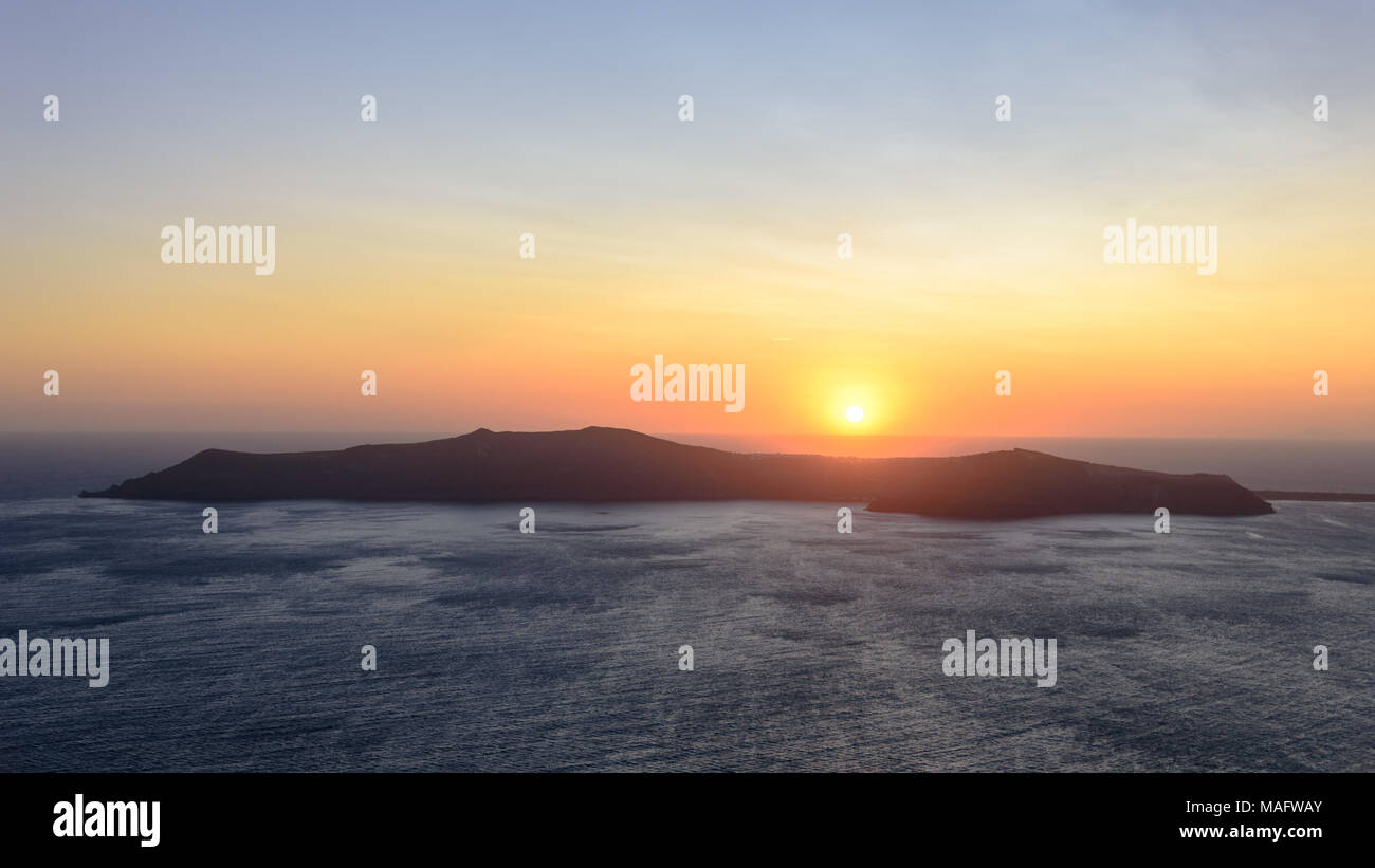 The sun setting behind Thirasia over the Aegean Sea Stock Photo