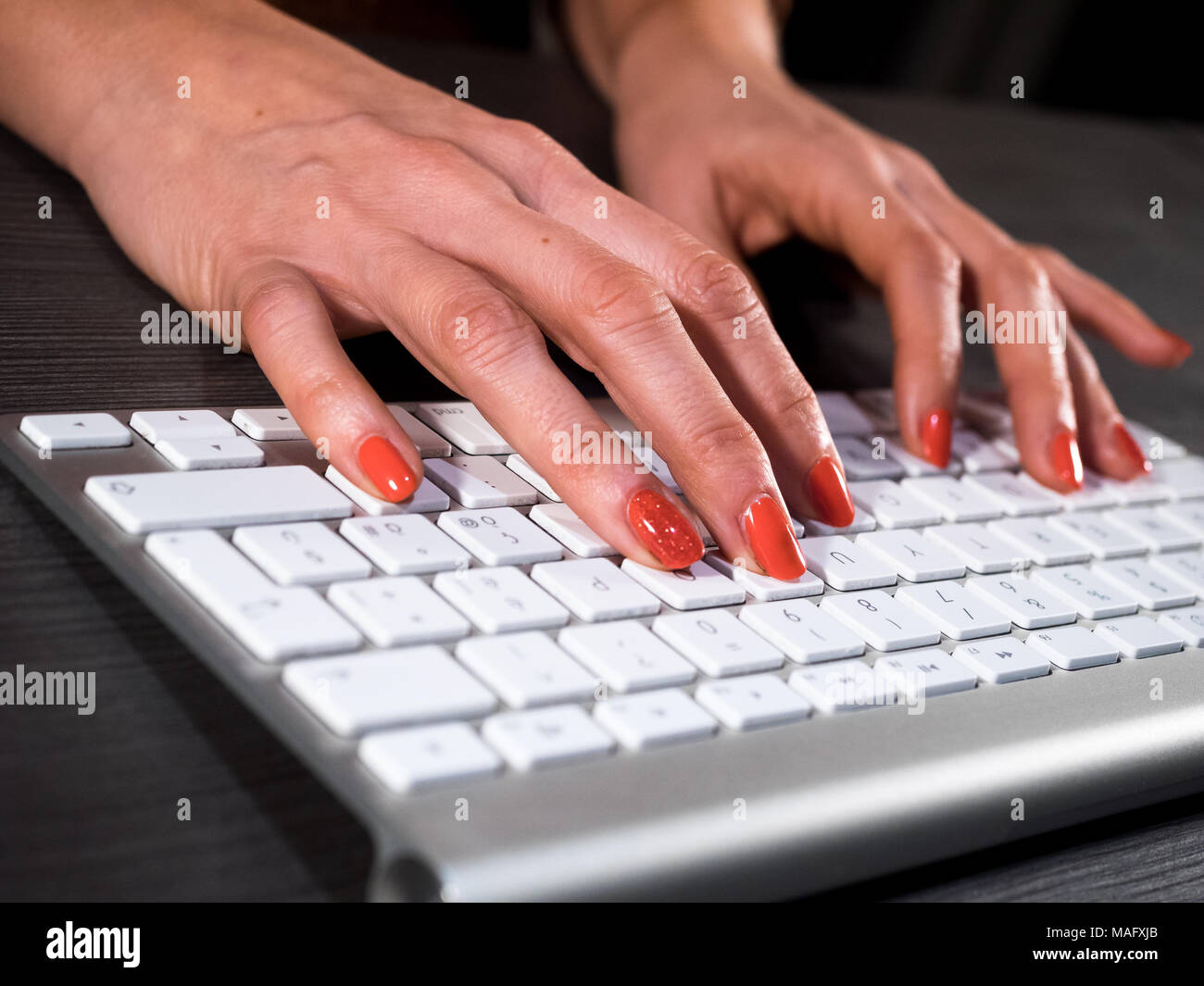 Woman with red nails typing on wireless keyboard Stock Photo