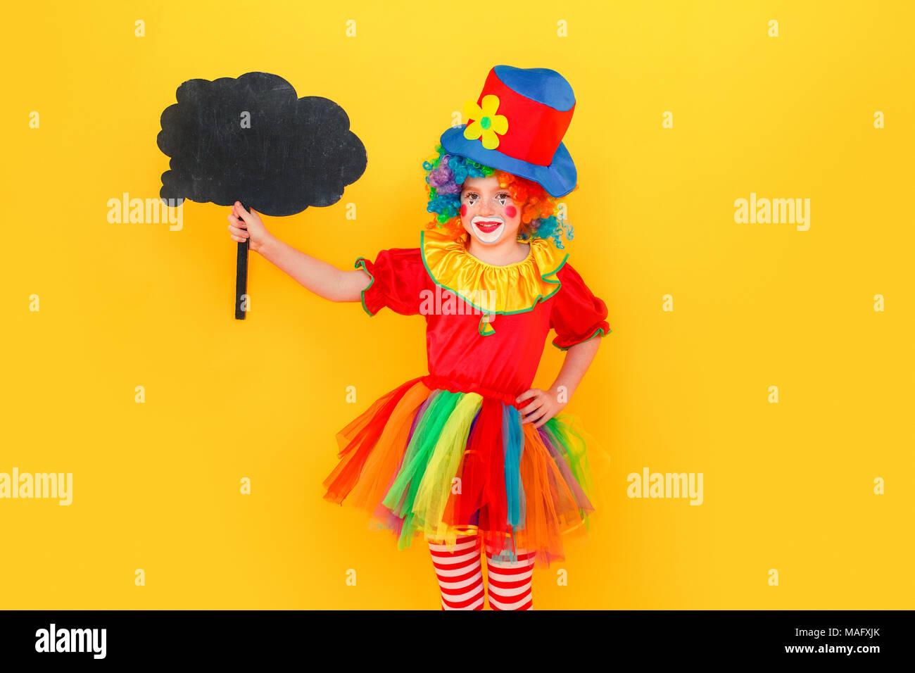 Happiness girl in clown costume and hat holding black table. Studio ...