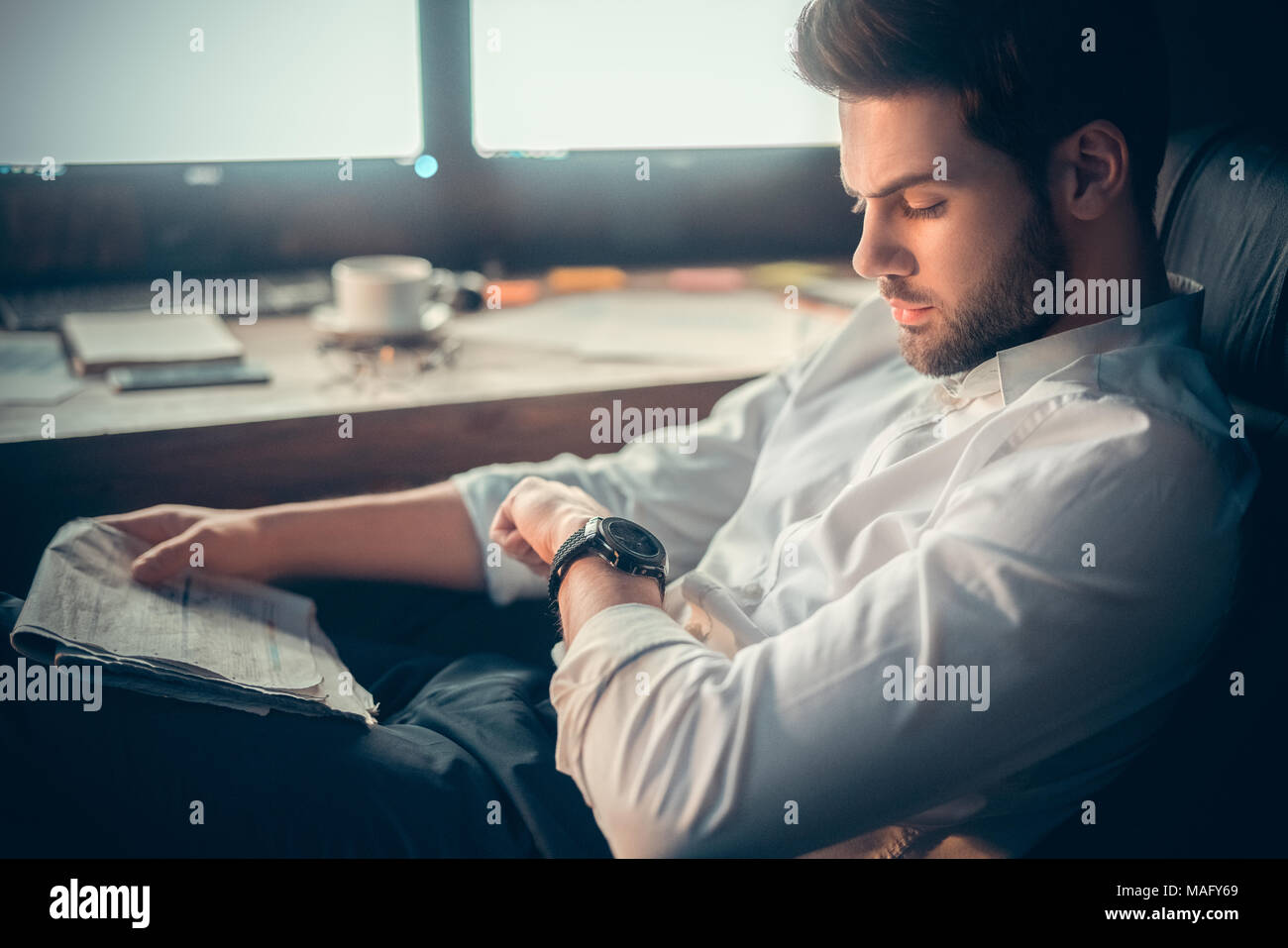 Young bearded man trader at office sitting at table looking at time staying late close-up Stock Photo