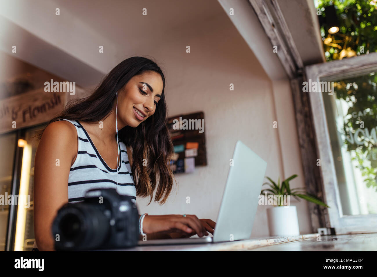 Woman blogger using laptop at home wearing earphones. Woman sitting with a professional camera on the table working on her laptop computer. Stock Photo
