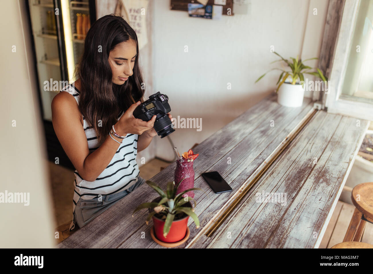 Woman taking photos of a smoothie placed beside a flower pot using a professional camera for her food blog. Food blogger shooting photos for her blog  Stock Photo