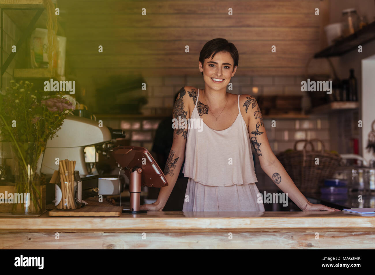 Woman standing at the counter of her cafe posing. Smiling restaurant owner standing beside the billing machine. Stock Photo