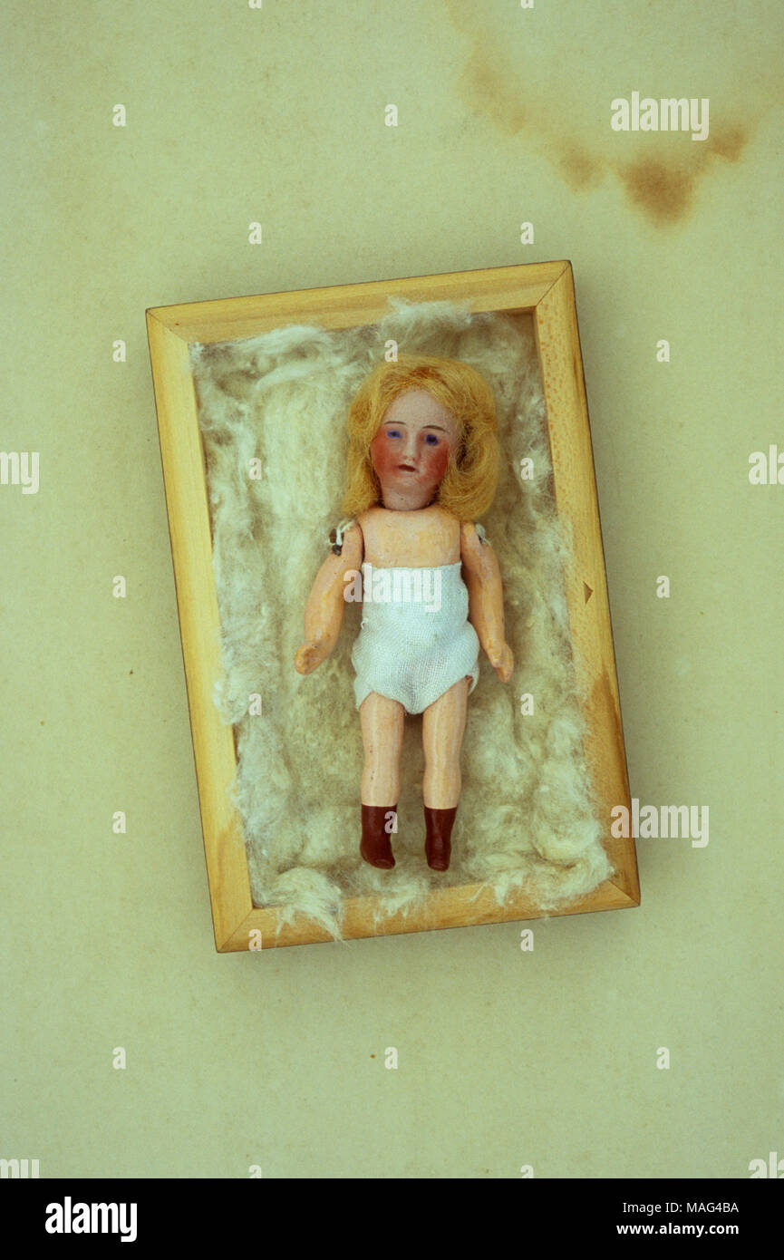 Antique doll with white underwear painted brown boots, red cheeks and blonde hair lying on cotton wool in box Stock Photo