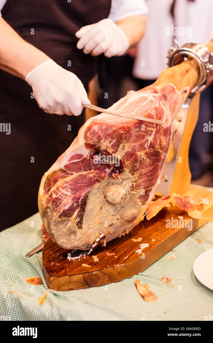 A front leg of Serrano ham also known as Spanish Iberian ham or Pata Negra mounted on a wooden stand with a butcher cutting slices of it Stock Photo